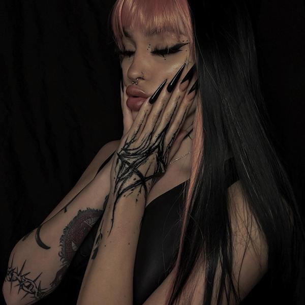 Person mit Handtattoo und langen Nägeln vor dunklem Hintergrund
